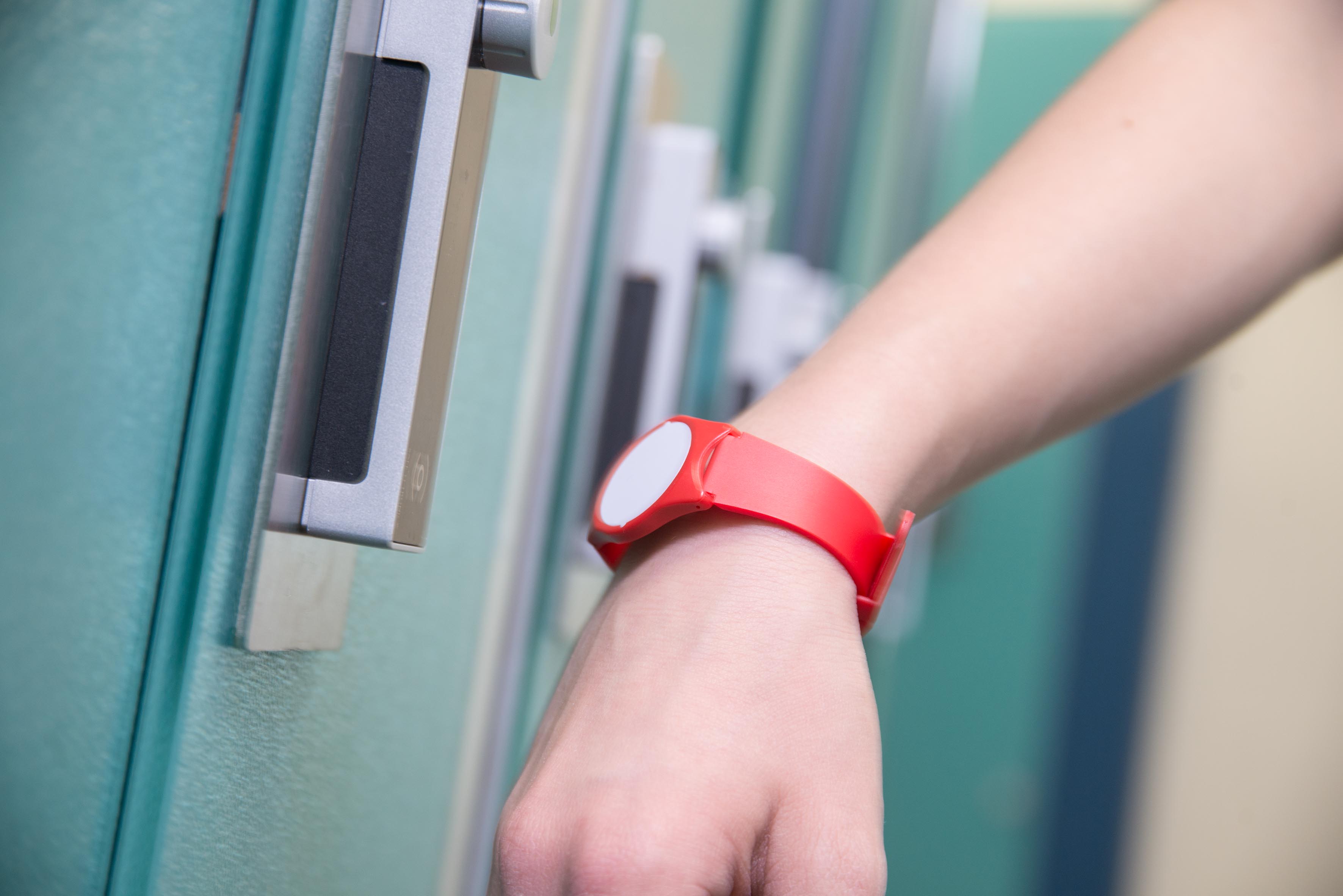 Hand mit rotem Armband hält vor einem elektronischen Türschloss an
